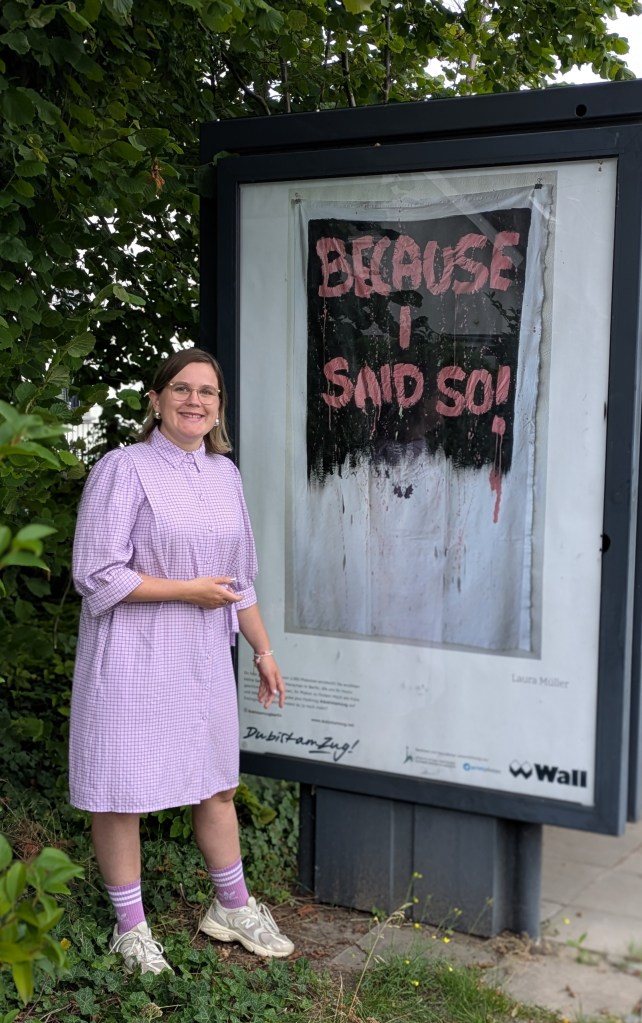 Laura Müller steht vor dem Plakat Ihres Werkes Because I Said so